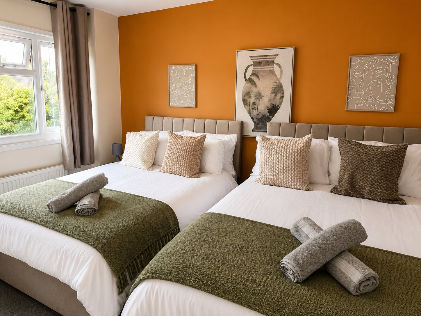 Twin bedroom with olive green blankets, cream pillows, orange accent wall and framed artwork