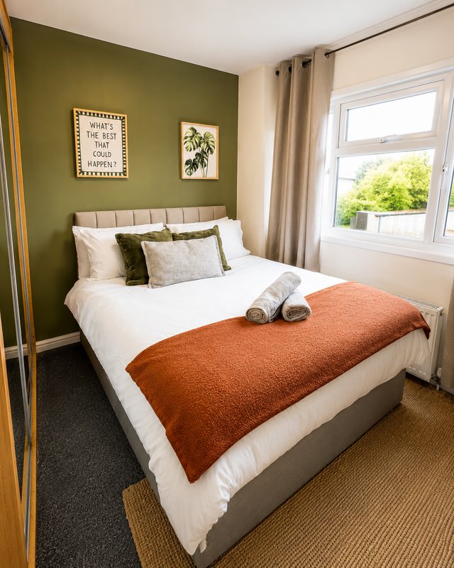 Modern bedroom with double bed, green feature wall, white bedding and orange throw blanket