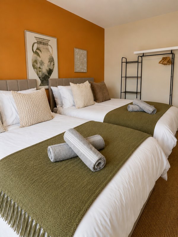 Bright bedroom with two single beds, olive green throws, orange accent wall and framed artwork