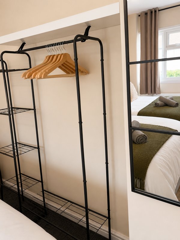 Bedroom with black metal clothing rack, wooden hanger, and bed with olive bedding visible