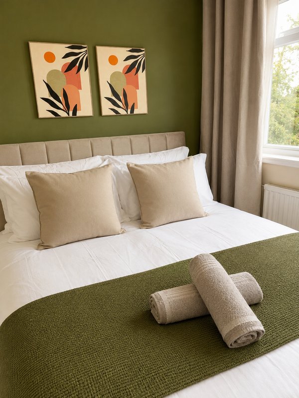 Bedroom with olive green walls, beige upholstered headboard, white bedding, and abstract art
