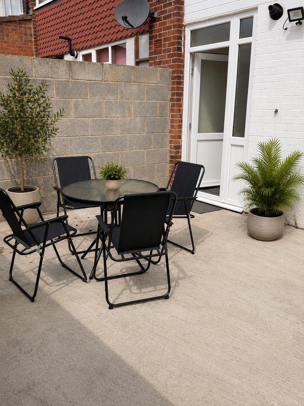 Outdoor patio with black dining set, potted plants, brick wall and white door