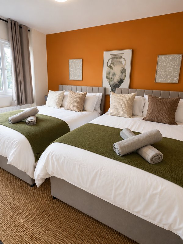 Twin bedroom with olive green throws, white pillows, orange accent wall and framed artwork