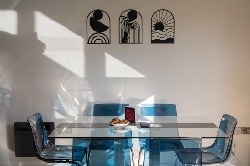 Modern dining area with glass table, blue chairs, and minimalist wall art