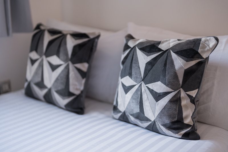 Bed with striped white sheet and two geometric patterned cushions in black and white