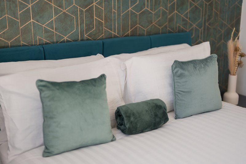 Bed with teal upholstered headboard, white bedding, and green velvet cushions