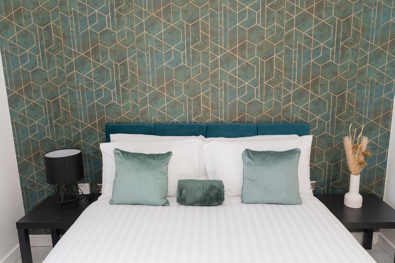 Modern bedroom with double bed, geometric teal wallpaper, white bedding and coordinating cushions