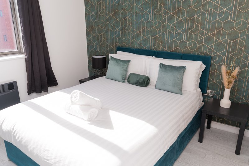 Modern bedroom with teal upholstered bed, white bedding, geometric patterned headboard and side table