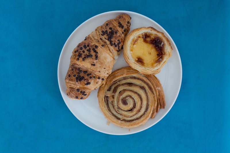 White plate with croissant, pastry tart, and spiral pastry on blue background