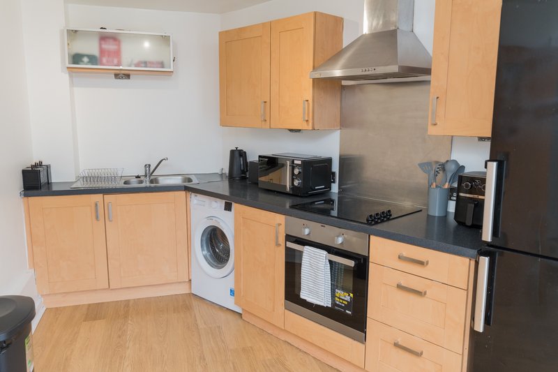 Kitchen with wooden cabinets, black countertop, integrated appliances and washing machine