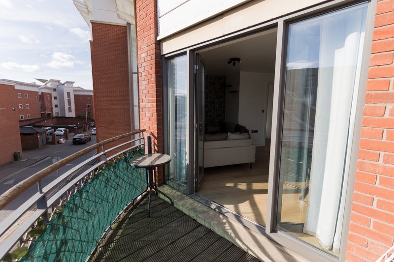 Modern brick building balcony with green railing, wooden decking, and glass sliding doors opening to interior room
