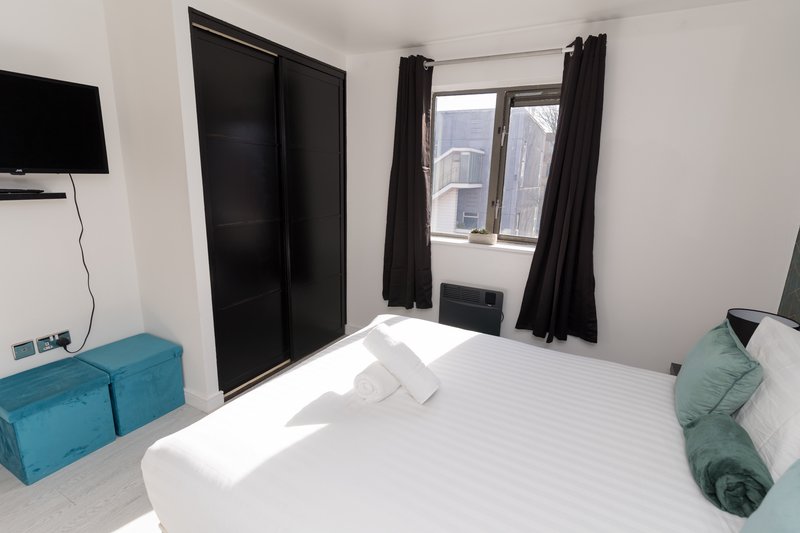 Modern bedroom with white bed, turquoise storage boxes, black wardrobe and window with city view