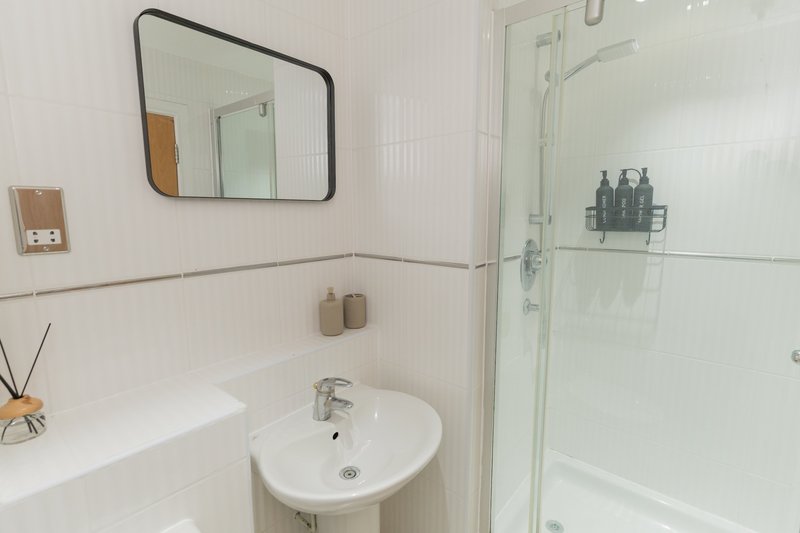 Clean modern bathroom with white sink, mirror, bathtub and glass shower enclosure