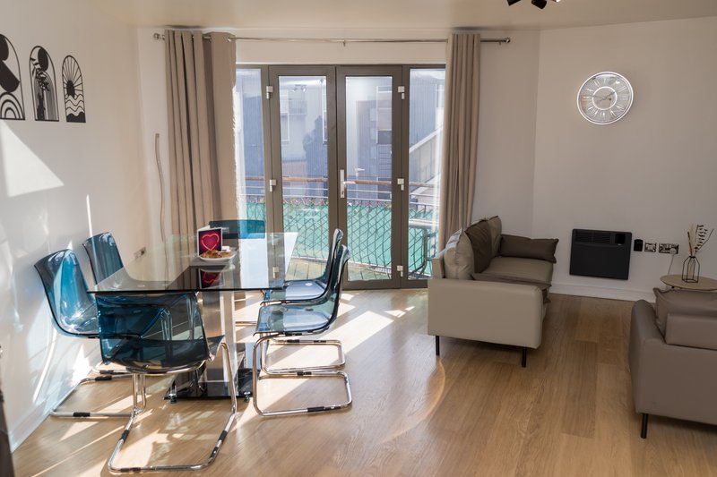 Modern living room with glass dining table, blue chairs, beige sofa and balcony doors