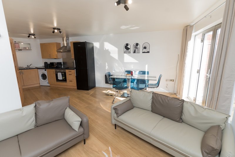 Open-plan living area with sofa, armchair, wooden flooring, kitchen with appliances and dining table