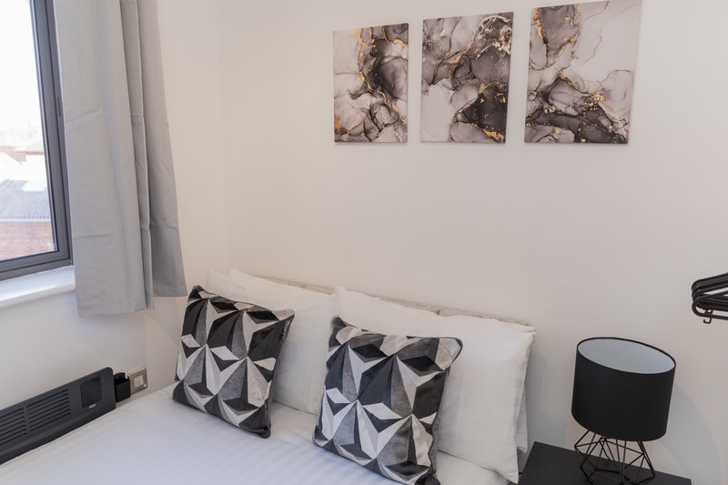 Bright bedroom with white bed, geometric patterned cushions, wall art and side lamp