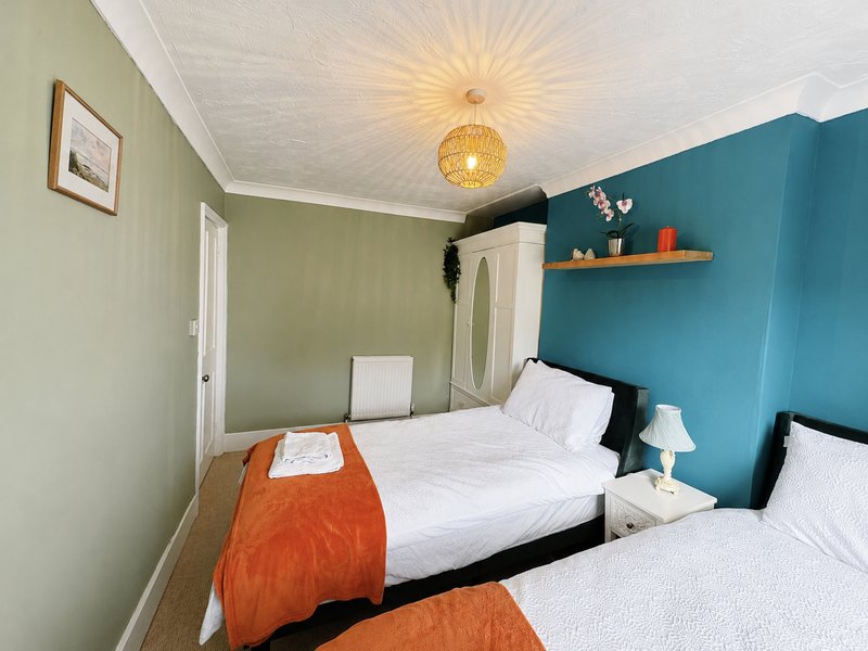 Bright twin bedroom with white beds, orange throws, teal and green walls, pendant light