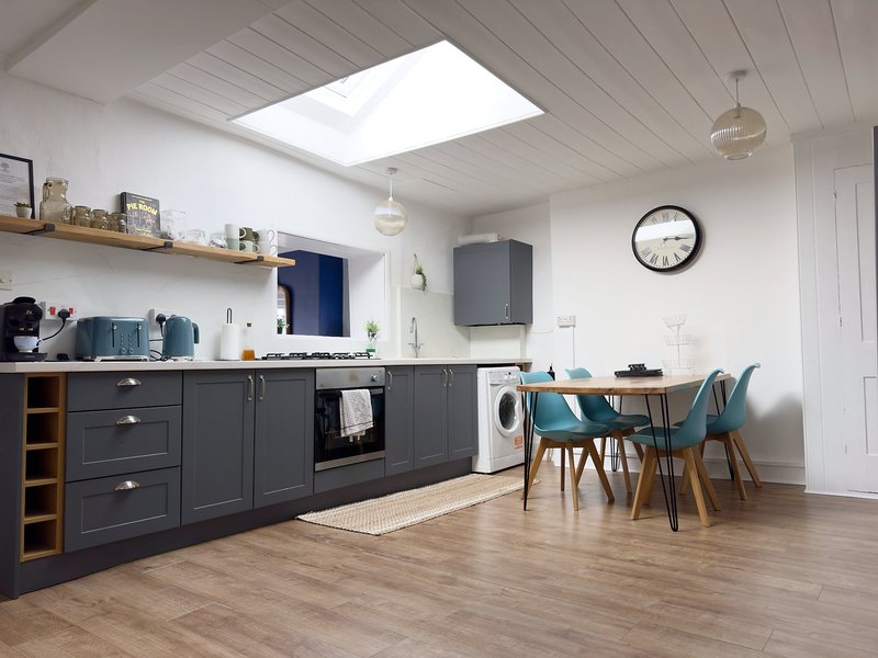 Modern kitchen and dining area with dark cabinetry, skylight, wooden dining table and blue chairs