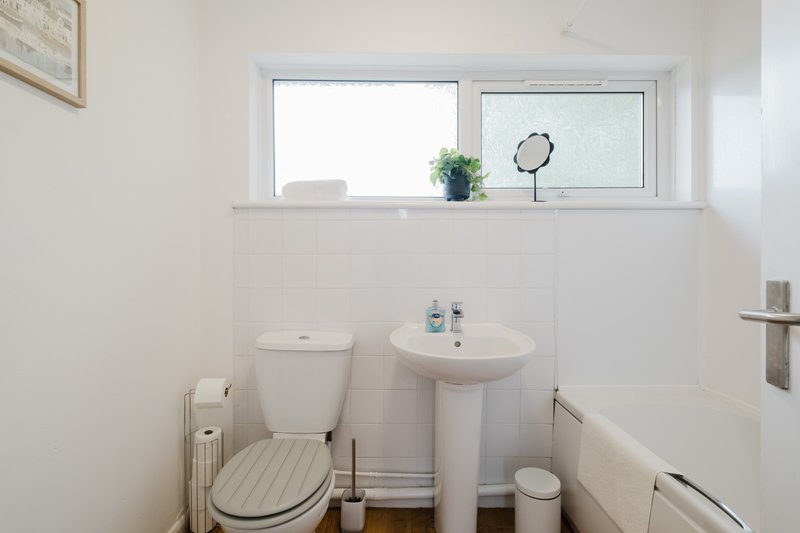 Small bathroom with toilet, pedestal sink, mirror and window with natural light
