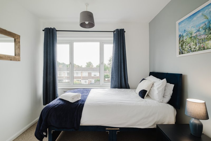 Modern bedroom with double bed, dark headboard, white bedding, blue curtains and window view