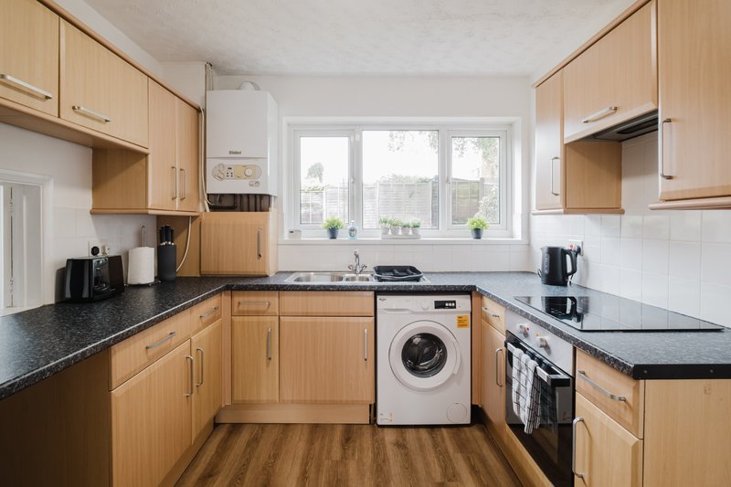 Modern kitchen with wooden cabinets, black countertops, washing machine and gas stove