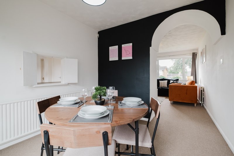 Open-plan dining and living area with round wooden table, black accent wall, and arched doorway