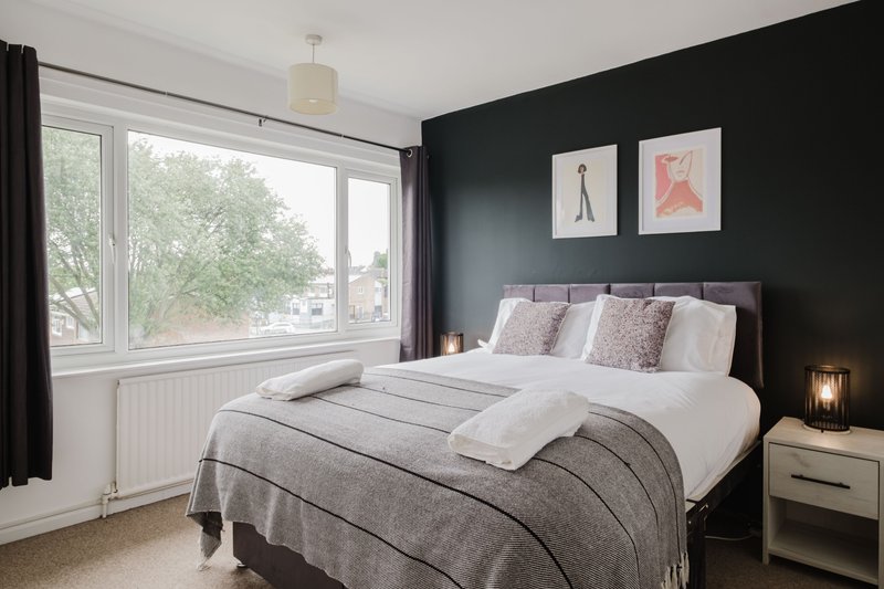 Modern bedroom with double bed, dark feature wall, large window and bedside furniture
