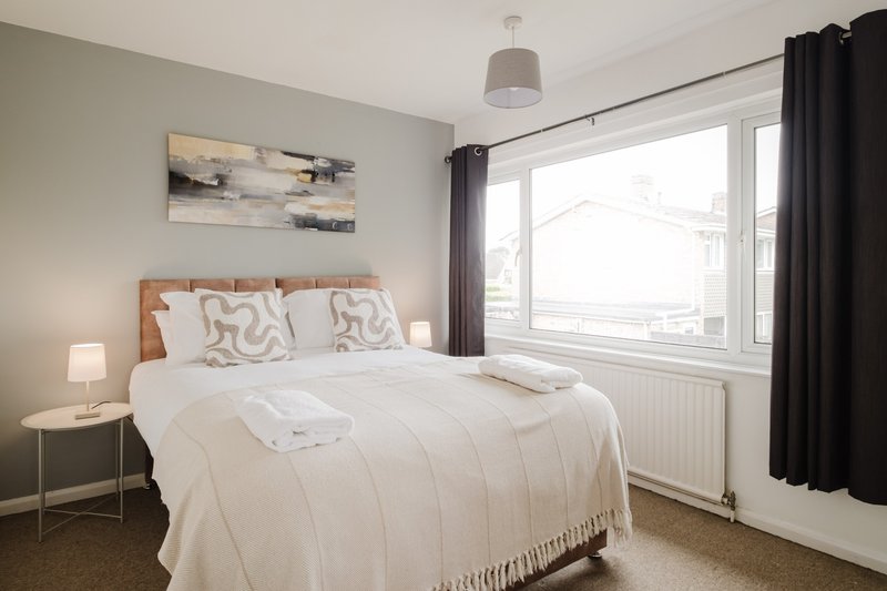 Bright bedroom with double bed, wooden headboard, white bedding, and large window with black curtains