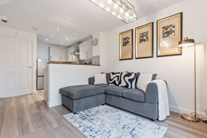 Modern open-plan living room with grey corner sofa, kitchen area, and framed wall art