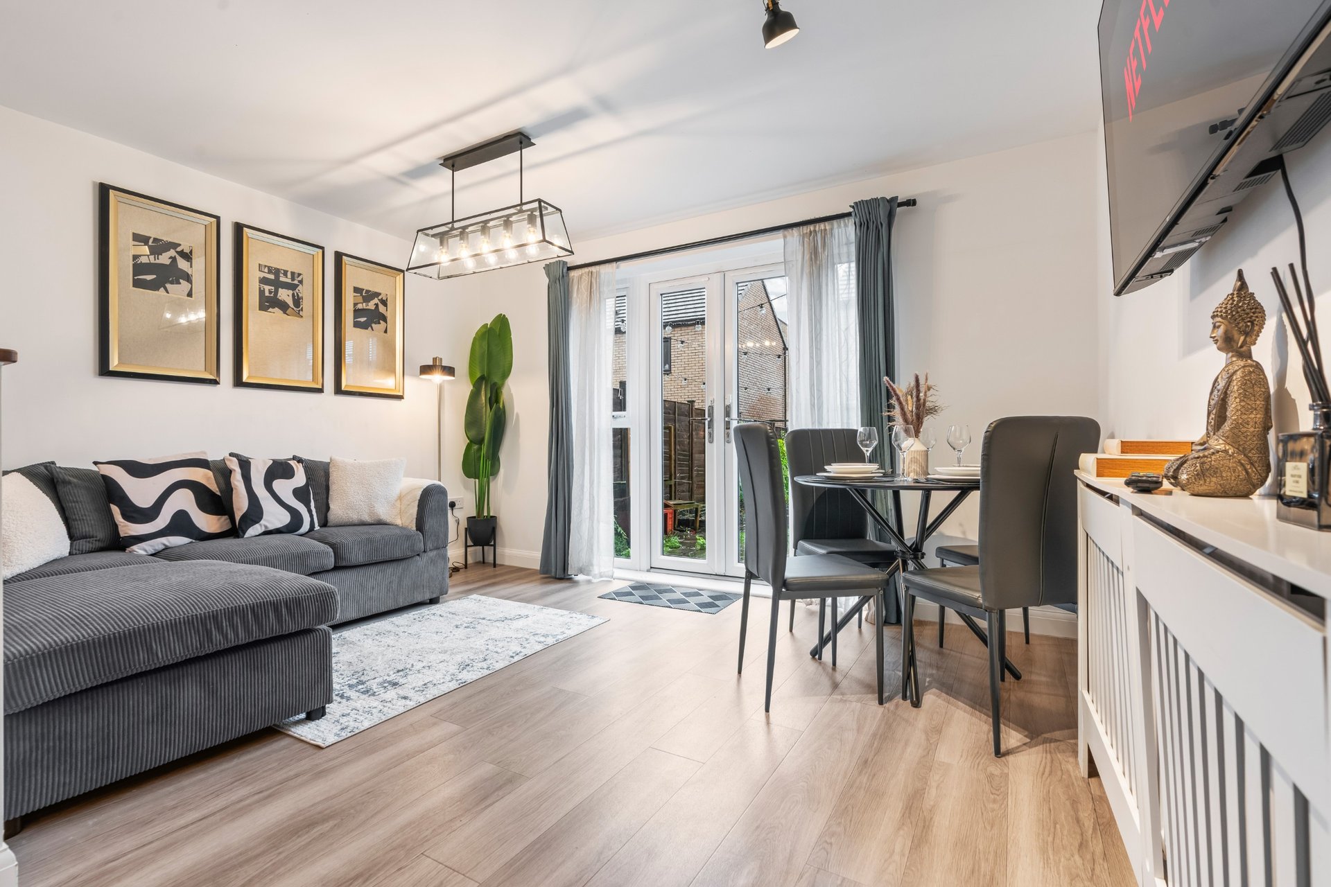 Modern open-plan living room with grey sofa, dining table, wooden flooring and garden doors