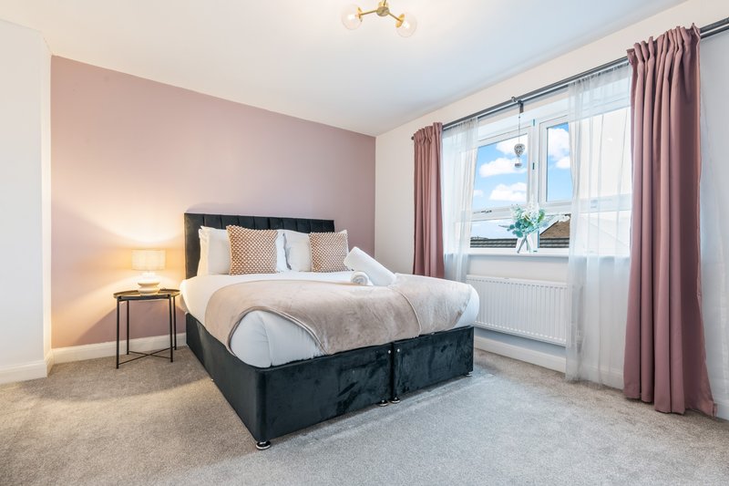 Modern bedroom with black bed frame, pink accent wall, bedside lamp, and large window with curtains