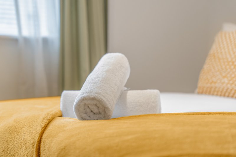 Rolled white towels arranged on yellow bedding in bright bedroom