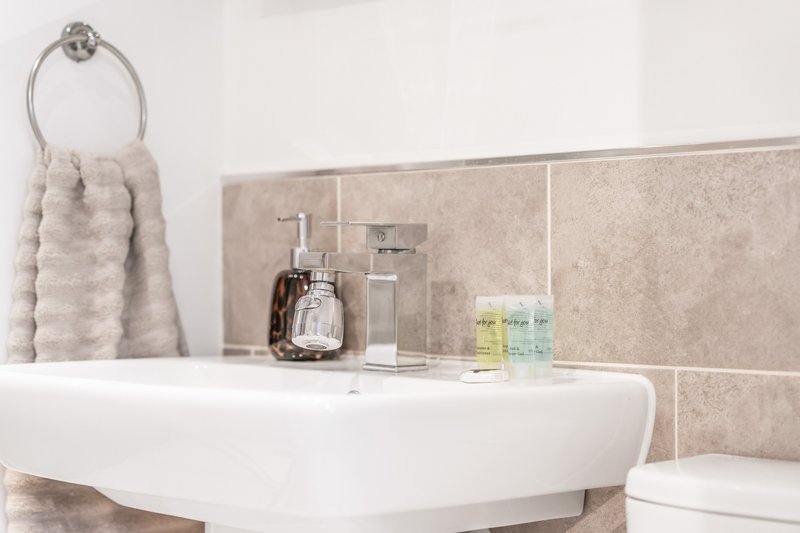 Modern bathroom with white pedestal sink, beige tile backsplash, towel ring, and toiletries