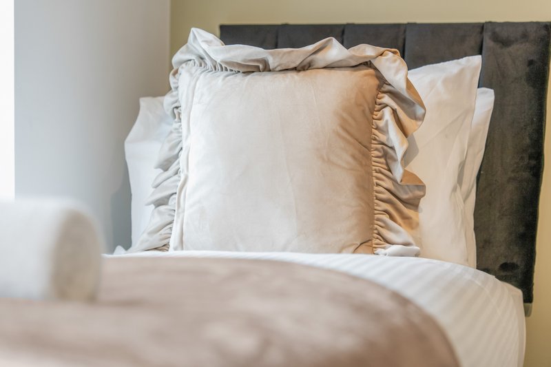 Bedroom with made bed, white pillows with ruffled edges, and dark headboard