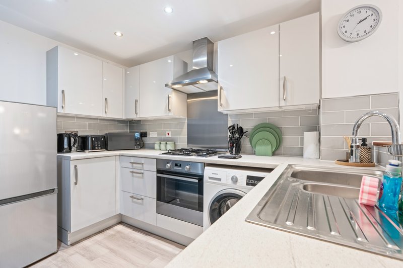 Modern white kitchen with stainless steel appliances, subway tile backsplash and clock