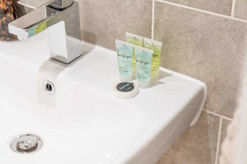 Modern bathroom sink with chrome tap, green toiletry bottles and white soap dish