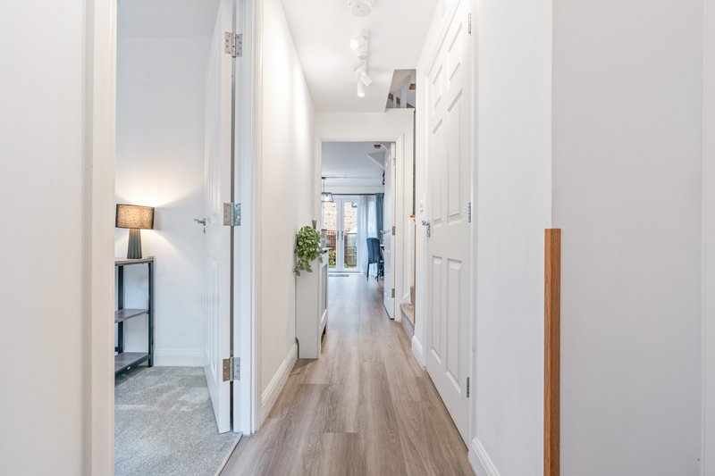 Bright hallway with white doors, wooden flooring, potted plant and side table lamp