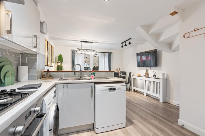 Modern open-plan kitchen with white cabinetry, stainless steel appliances and wooden flooring