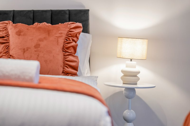 Modern bedroom with gray headboard, orange decorative pillows, white bedding, and bedside lamp
