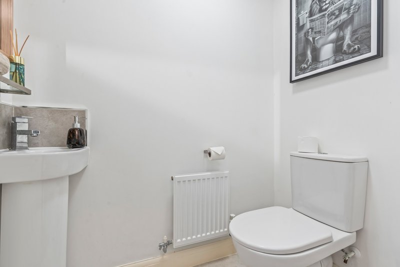 Compact bathroom with white toilet, sink, radiator and framed wall art