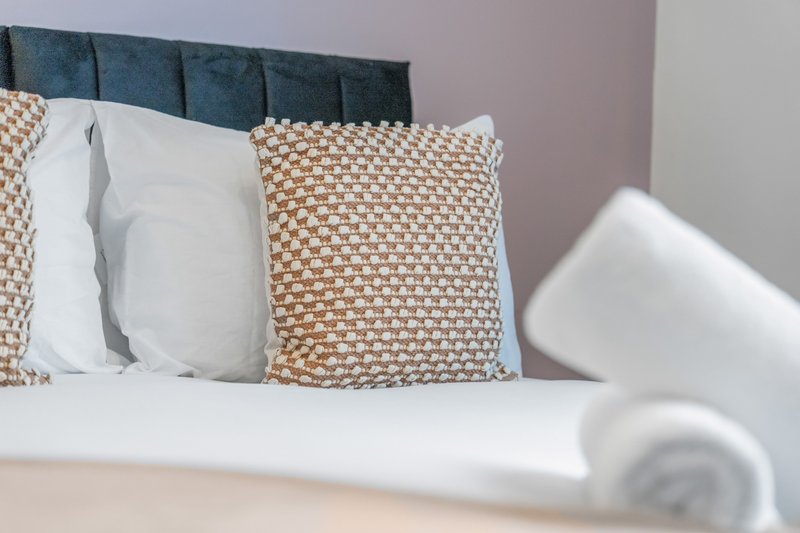 Bedroom with upholstered headboard, white pillows and patterned cushions on bed