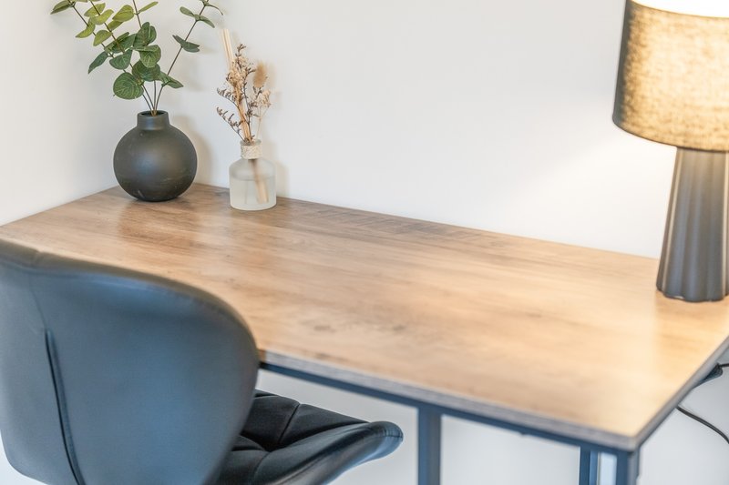 Wooden desk with blue chair, vases with greenery, and table lamp