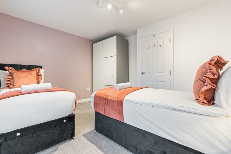 Twin bedroom with two beds, orange bedding, pink walls, white wardrobe and doors