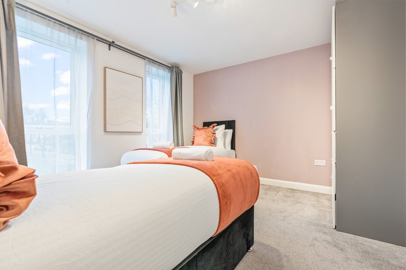 Modern bedroom with white bedding, orange accent throw, pink walls and large window with city views