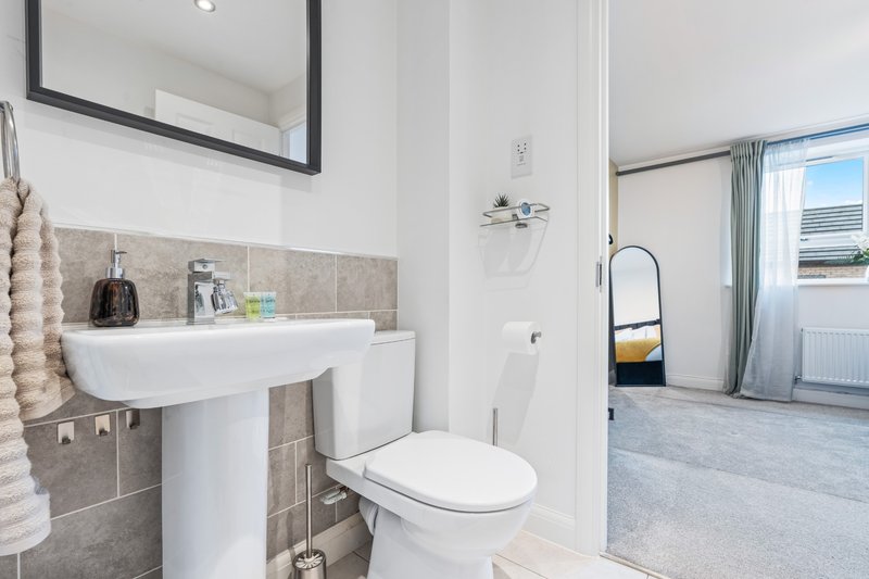 Clean bathroom with pedestal sink, toilet, beige tile backsplash and mirror