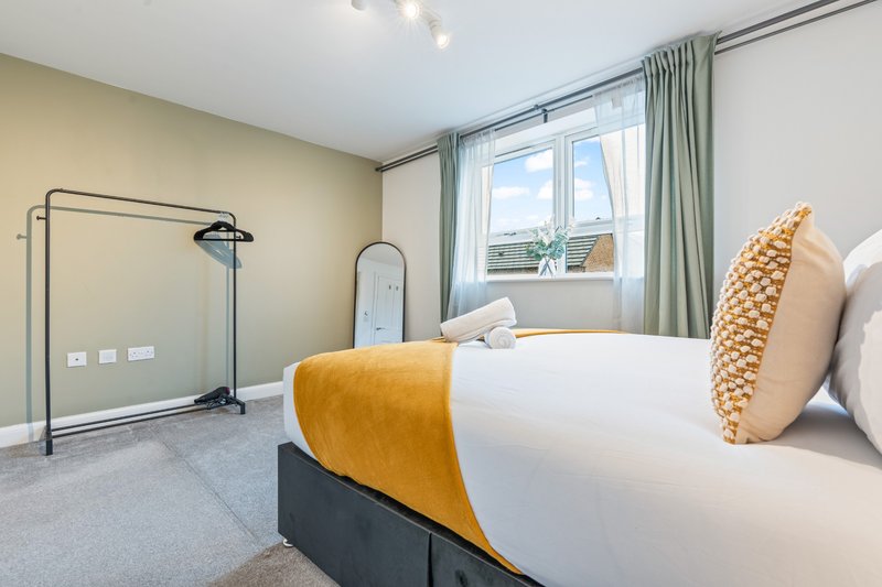 Modern bedroom with double bed, yellow throw, decorative pillows and large window