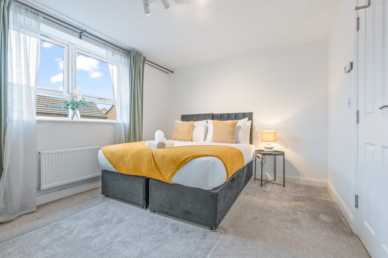 Bright bedroom with double bed, yellow bedding, large window with garden view, and bedside lamp