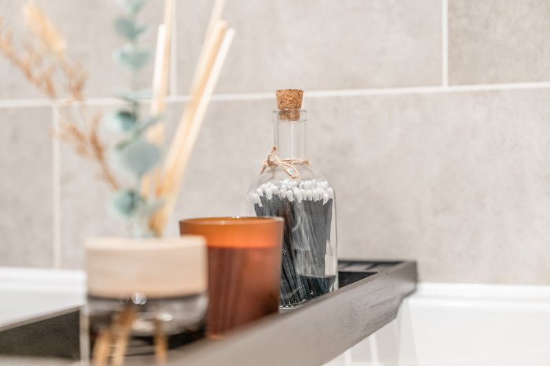 Bathroom counter with decorative bottles, candles, and dried flowers in vase