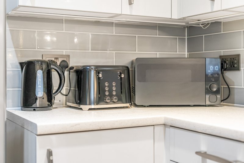 Modern kitchen counter with kettle, toaster, microwave and small appliances on white worktop
