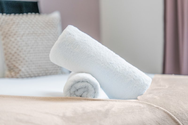 Rolled white towels arranged on a bed with decorative pillows and curtains visible